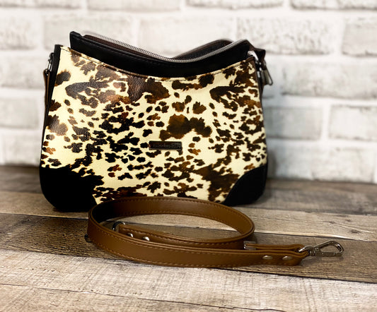 Brown cow print handbag with black faux leather accents. Front view showing the zipper panel open.