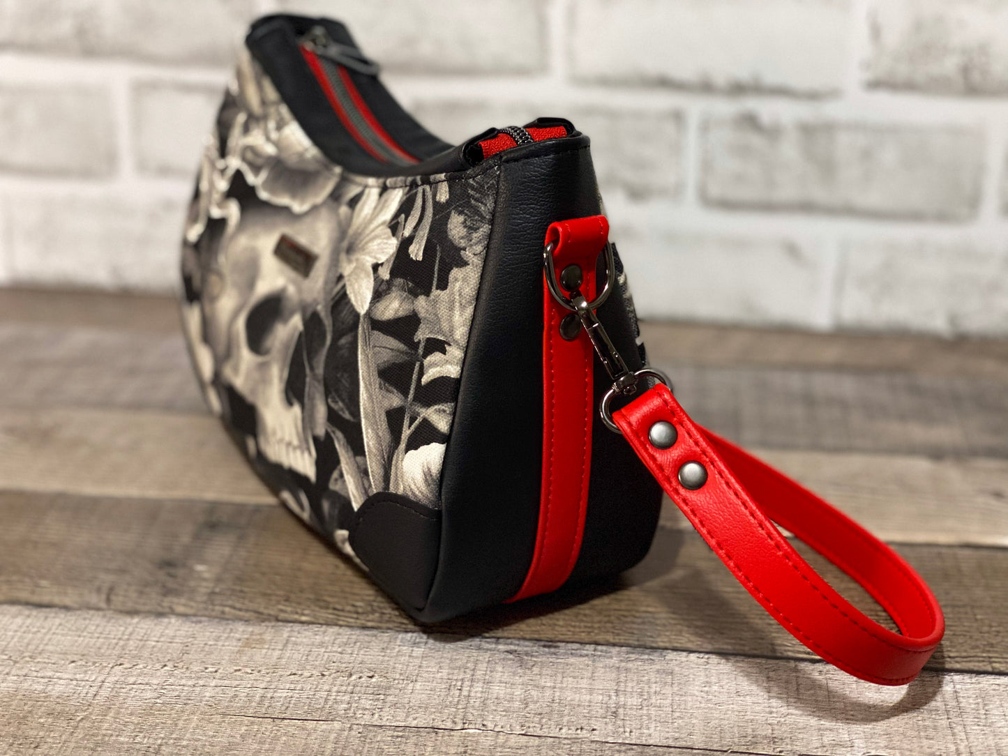 Handbag with skull and floral design with black and red faux leather accents. Side view,