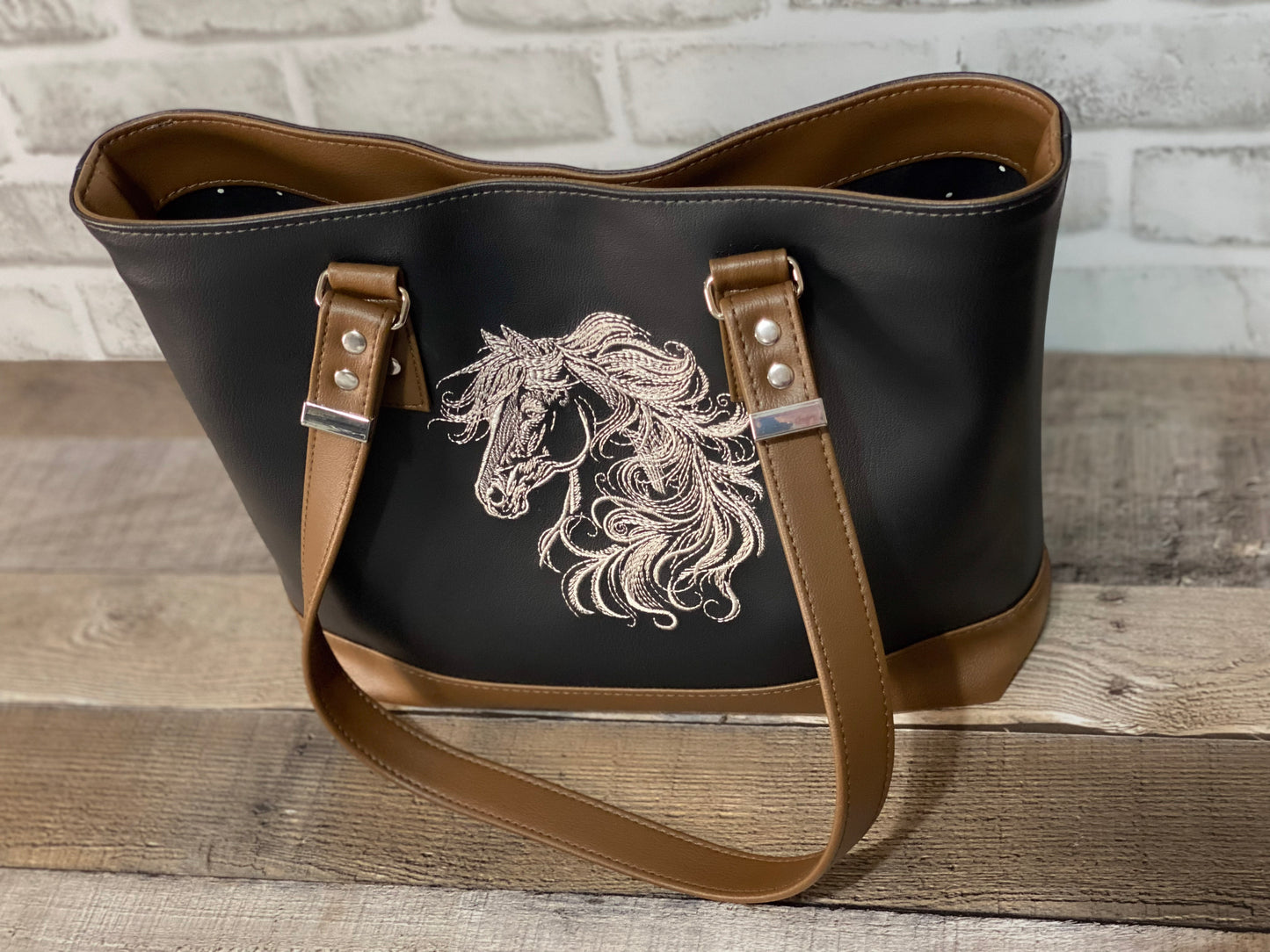 Black faux leather with brown accent straps. and bottom with embroidered horse head. Front view.