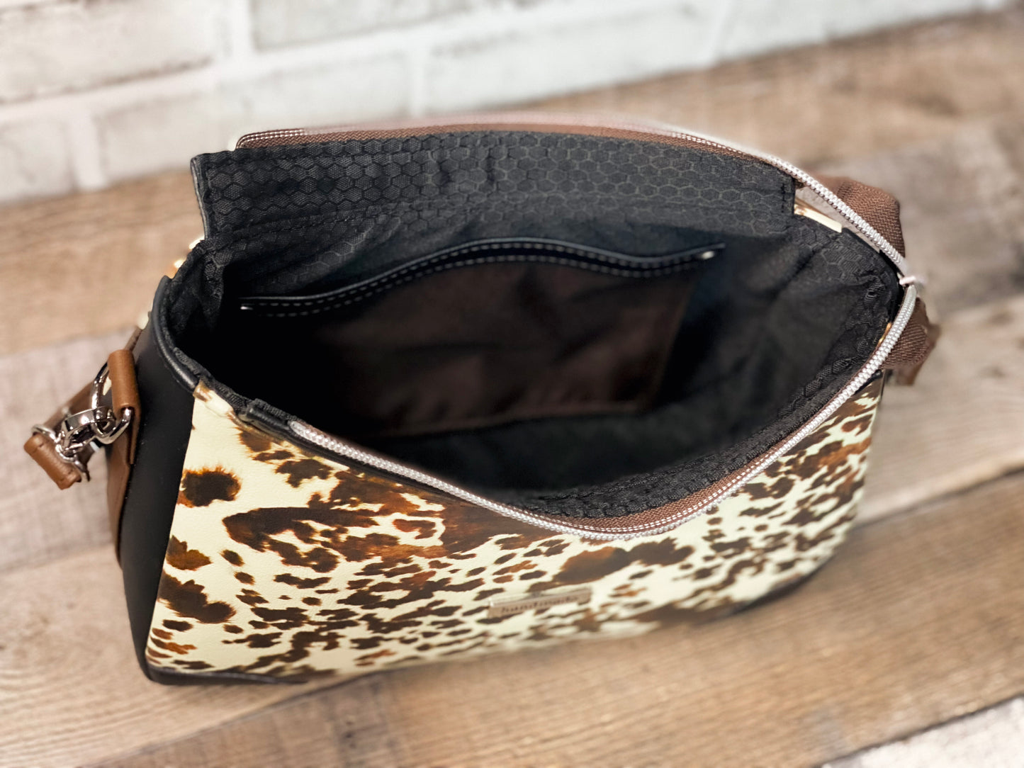 Brown cow print handbag with black faux leather accents. Inside view.