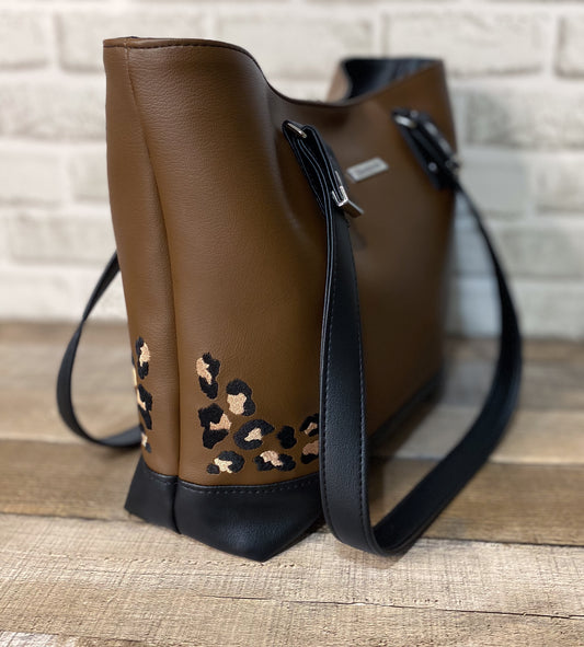 Brown faux leather handbag with leopard print accents on a wooden surface.
