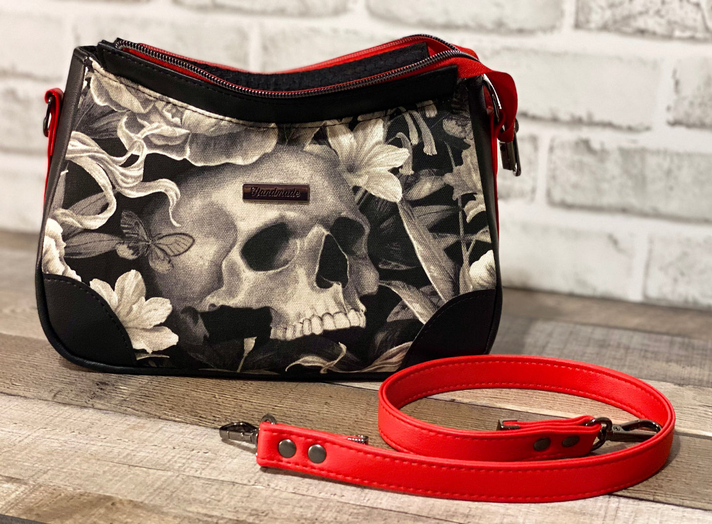 Handbag with skull and floral design with black and red faux leather accents.  Front view with open zipper