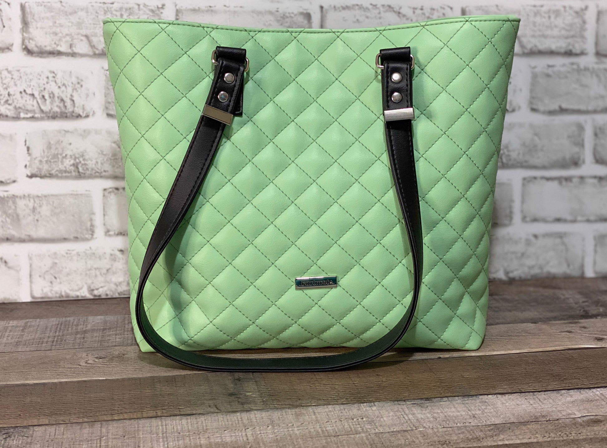 Mint green quilted handbag with black straps. Front Panel