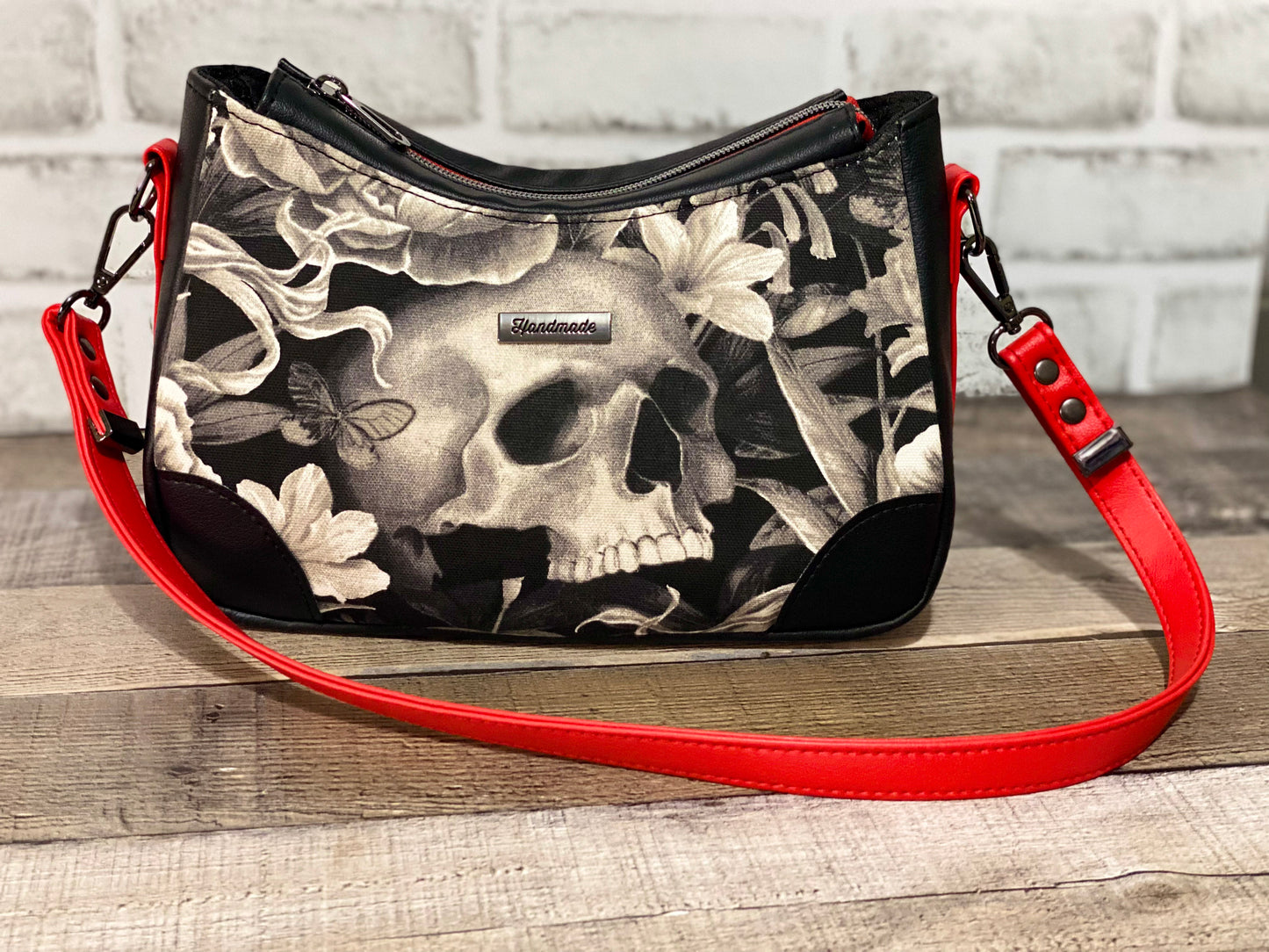 Handbag with skull and floral design with black and red faux leather accents.  Front view