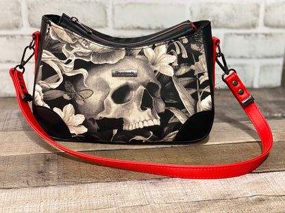 Handbag with skull and floral design with black and red faux leather accents.  Front view
