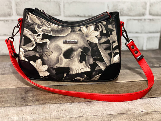 Handbag with skull and floral design with black and red faux leather accents.  Front view