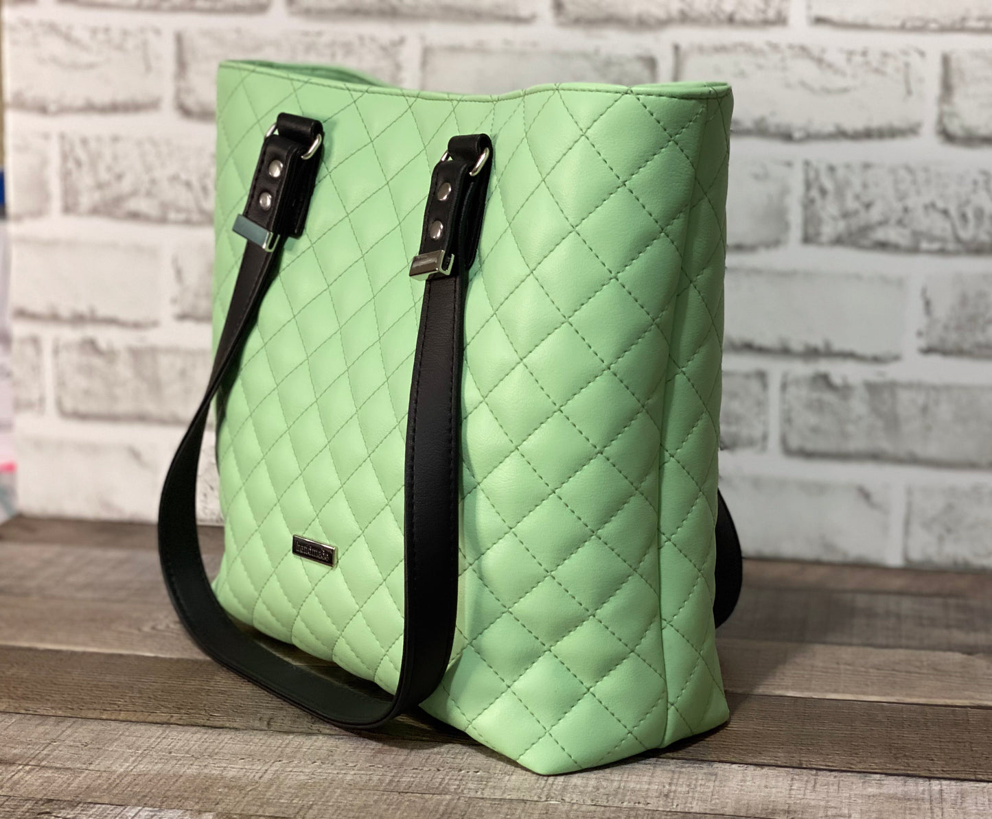 Mint green quilted handbag with black straps. Side View