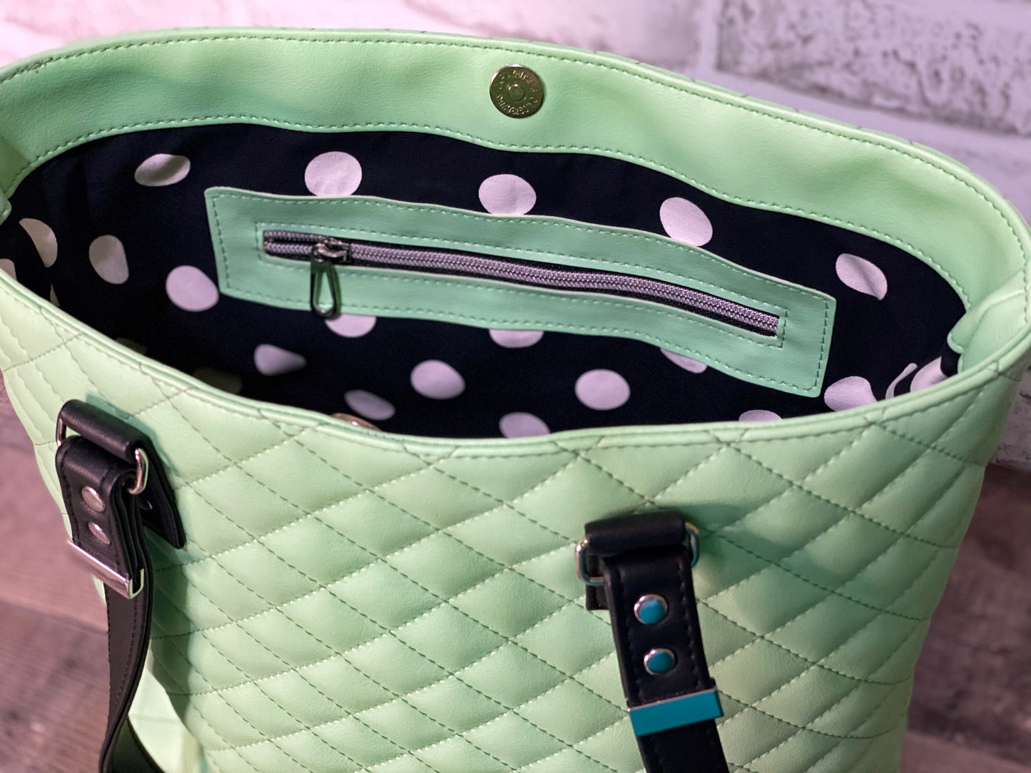 Mint green quilted handbag with black straps showing polkadot cotton lining. 