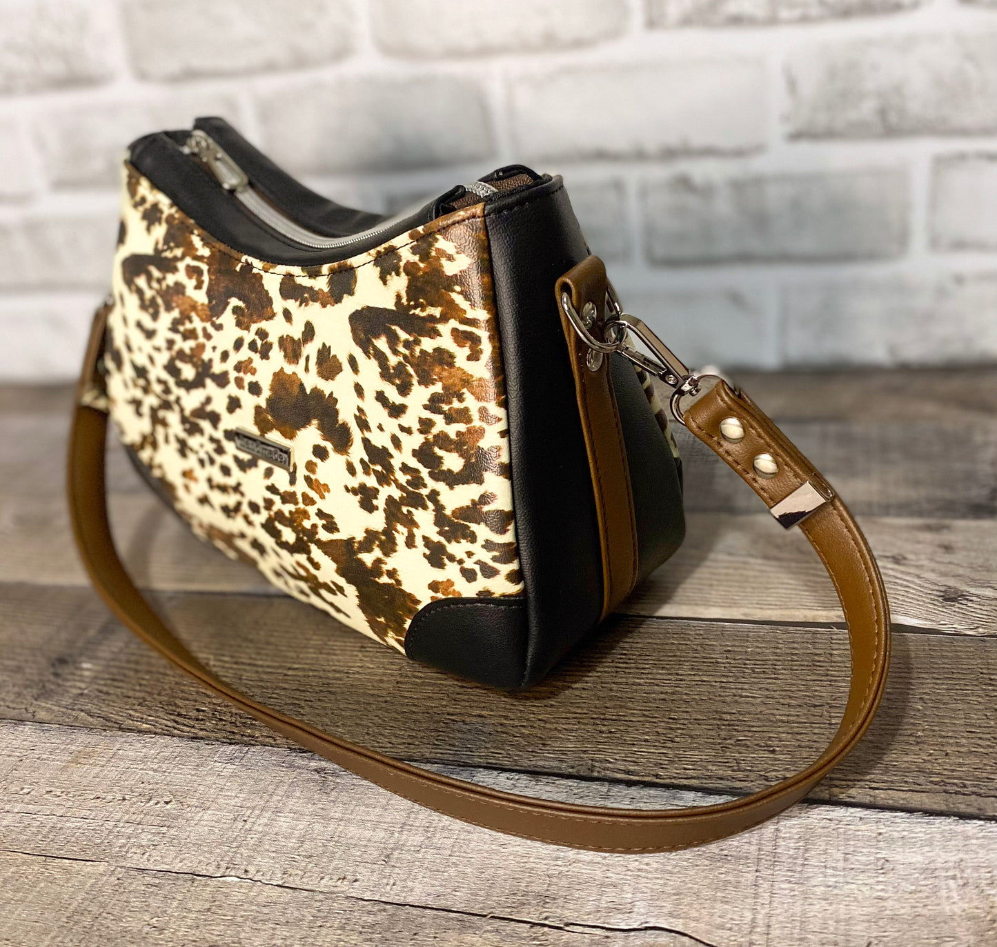 Brown cow print handbag with black faux leather accents. Side view. 