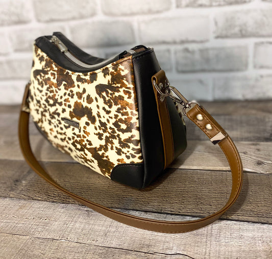 Brown cow print handbag with black faux leather accents. Side view. 