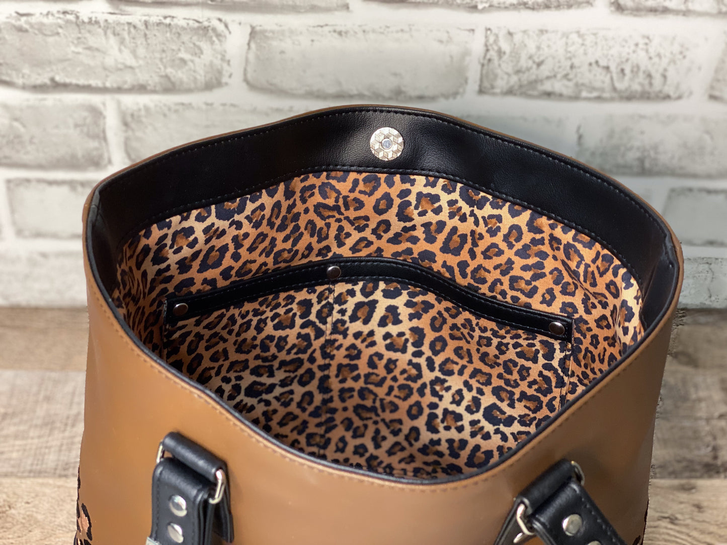 Brown handbag with leopard print interior against a brick wall background