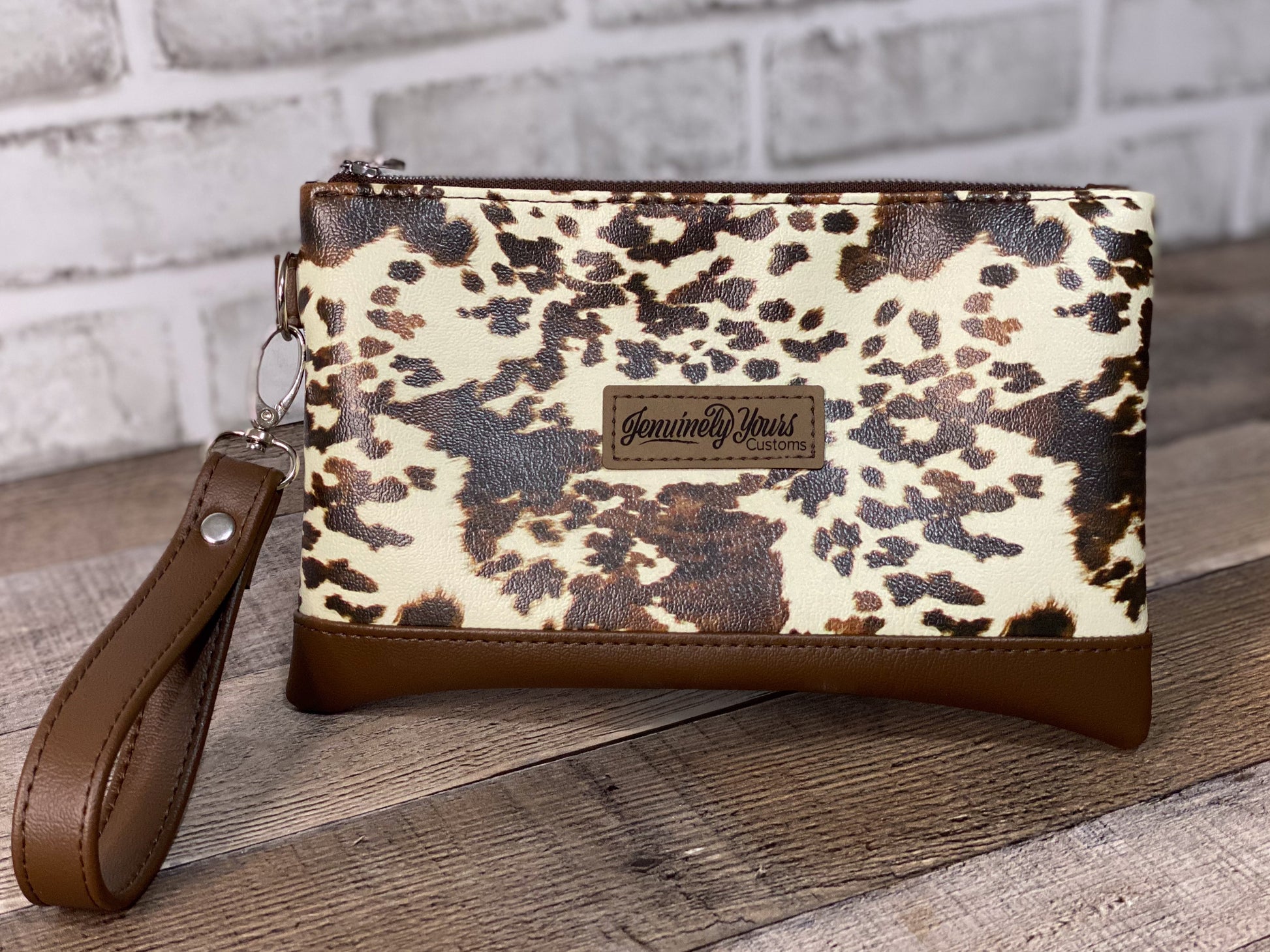 Cow print wristlet with brown strap on a wooden surface