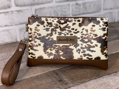 Cow print wristlet with brown strap on a wooden surface