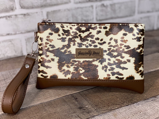 Cow print wristlet with brown strap on a wooden surface