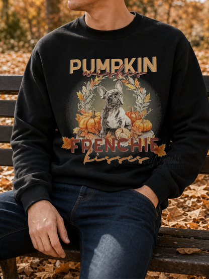 A person sitting on a bench outdoors wearing a black crewneck sweatshirt with a graphic print featuring a French Bulldog, pumpkins, and autumn leaves.