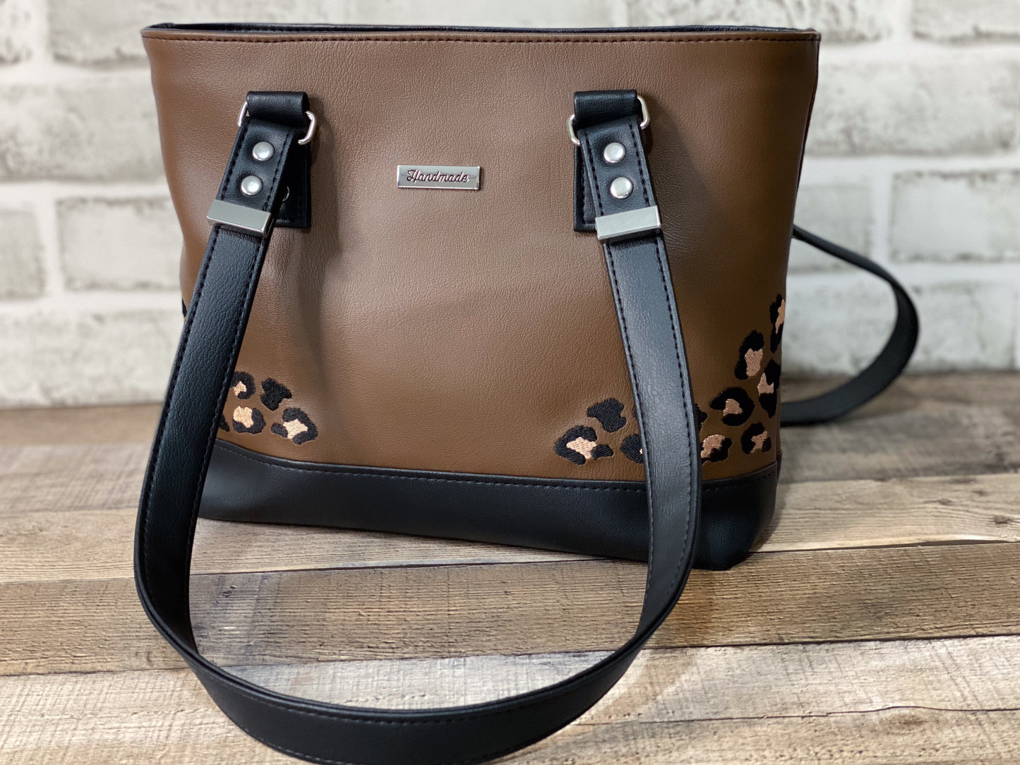 Brown handbag with black straps and leopard print accents on a wooden surface.