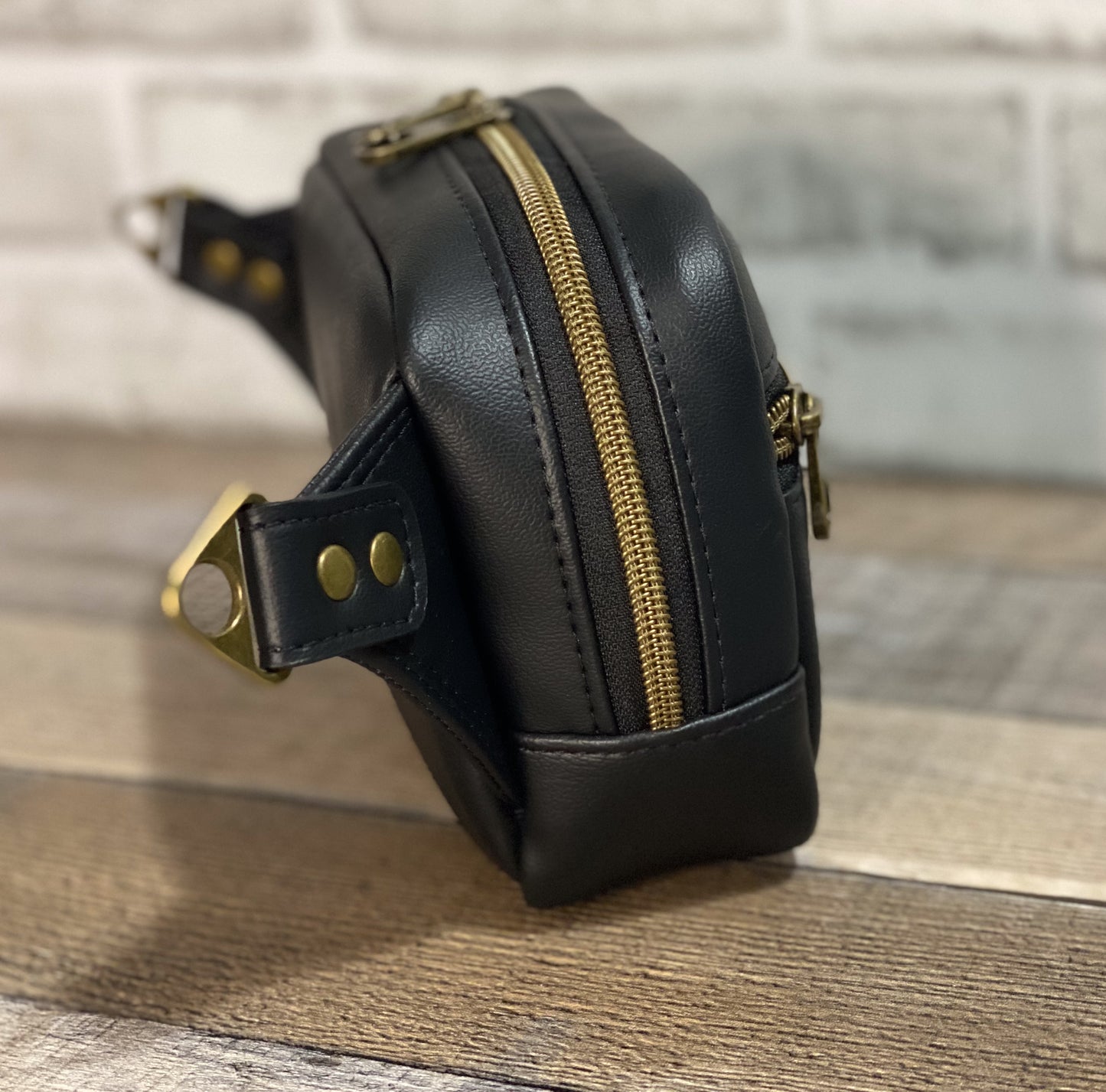 Side view of black faux leather hip back with antique gold hardware. 