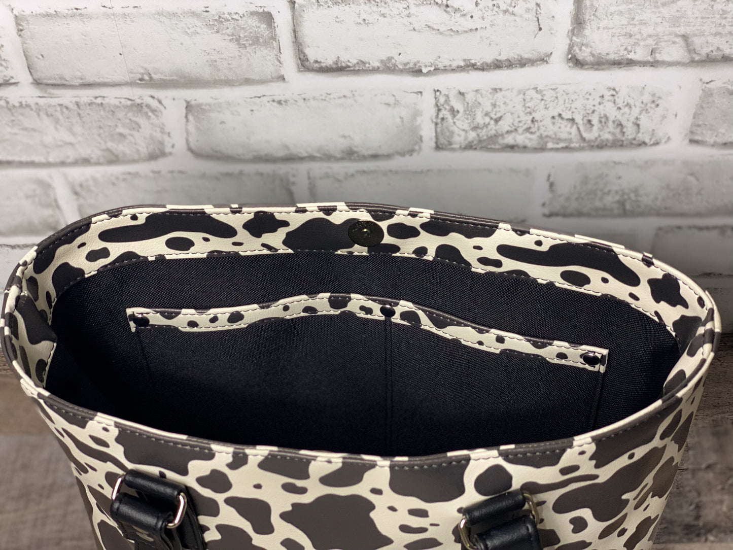 Black and white cow print big b tote bag interior view showing double slip pocket with cow accent piece. 