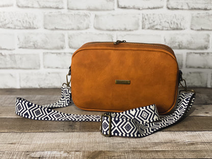 Rust orange crossbody bag with navy blue and white webbing for the strap. 