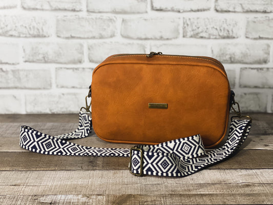 Rust orange crossbody bag with navy blue and white webbing for the strap. 