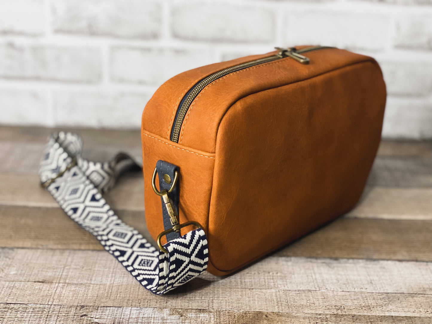 Rust orange crossbody bag with navy blue and white webbing for the strap.  Side view