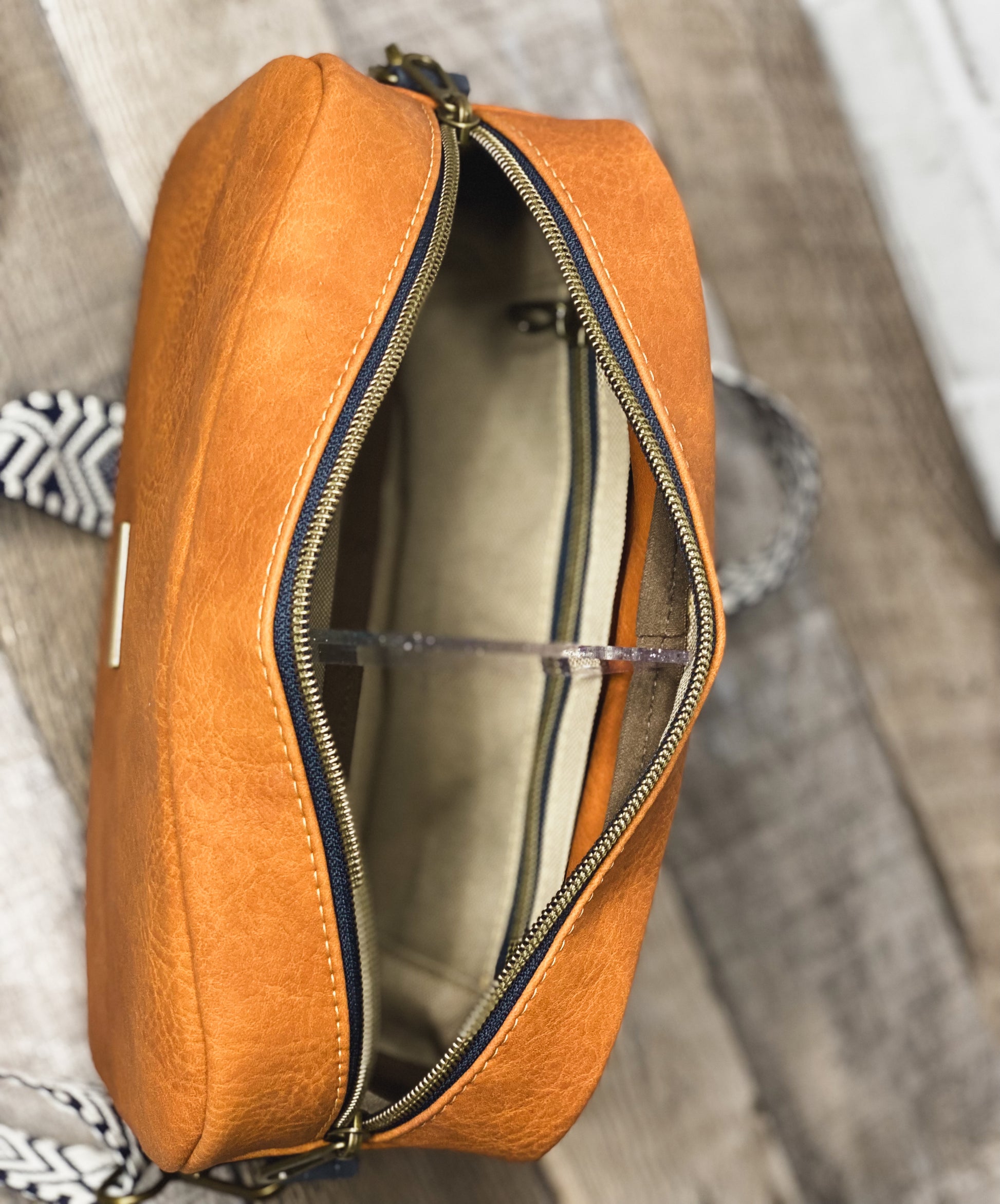 Rust orange crossbody bag with navy blue and white webbing for the strap. Showing the interior zipper pocket with a slip pocket. 