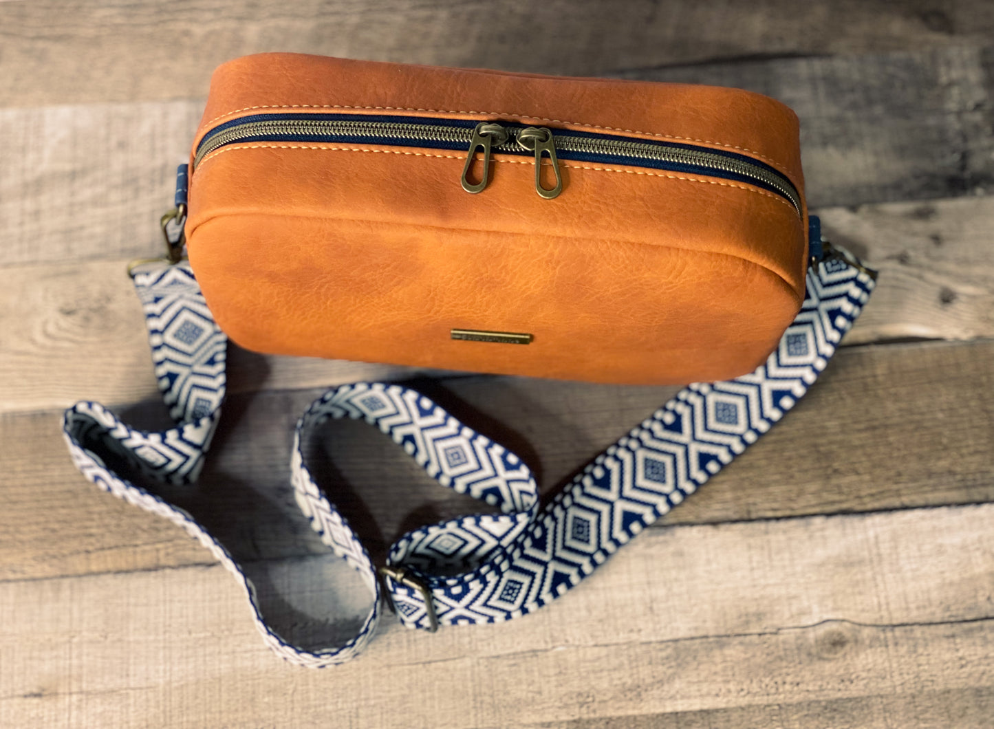 Rust orange crossbody bag with navy blue and white webbing for the strap.  Top view