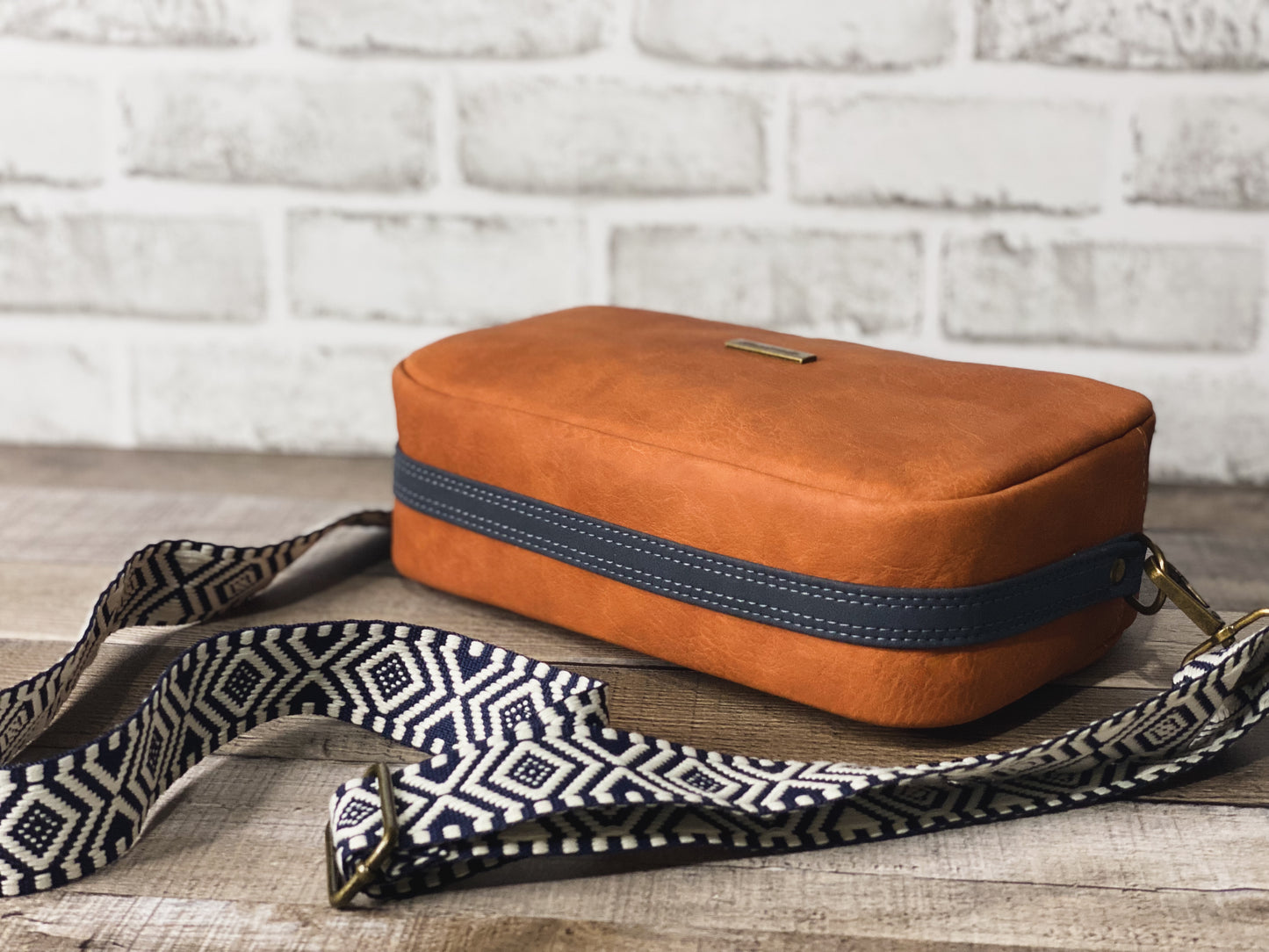 Rust orange crossbody bag with navy blue and white webbing for the strap.  - Side view