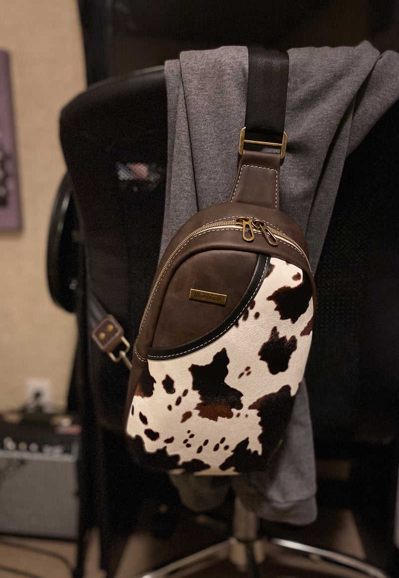 Brown and white cow print sling bag on a chair with an accent cow front pocket. 