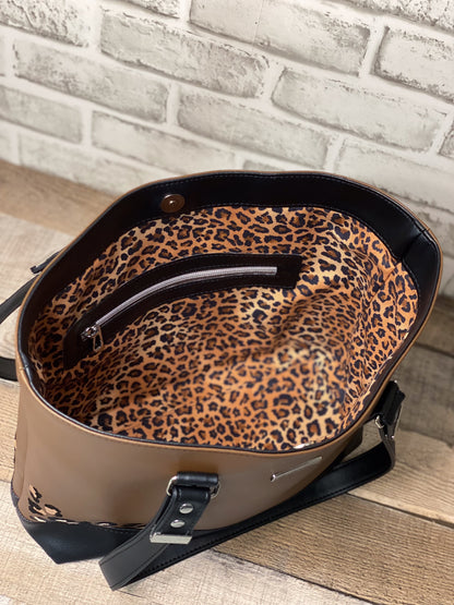Brown handbag with leopard print interior against a brick wall background