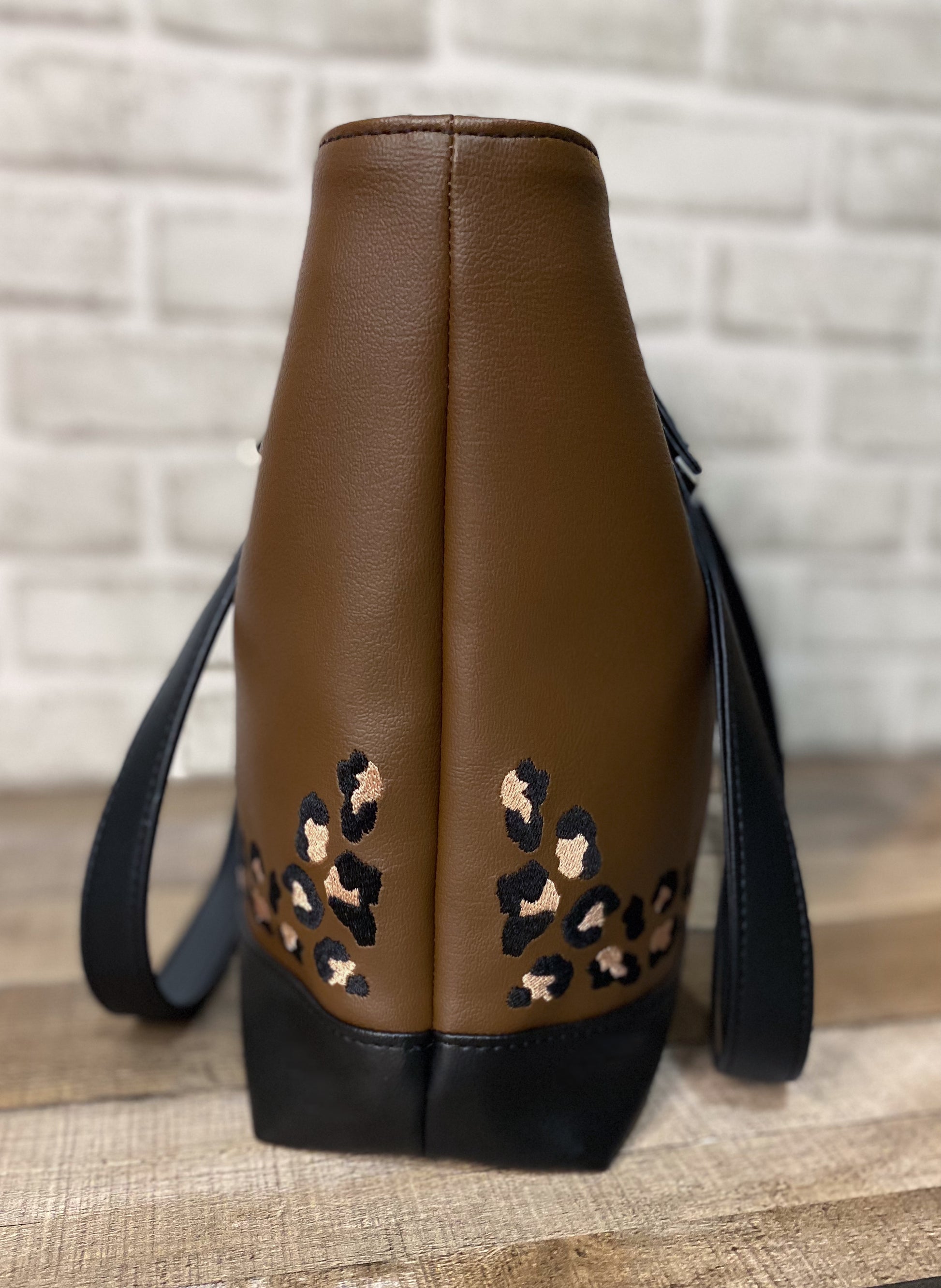 Brown faux leather bag with embroidered leopard print accents on a wooden surface.