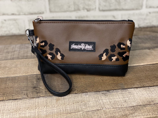Brown wristlet with leopard print accents and a visible brand label on a wooden surface.