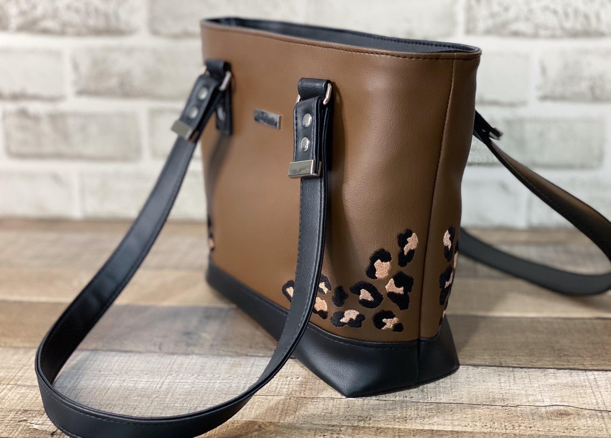 Brown handbag with embroidered leopard print accents on a wooden surface