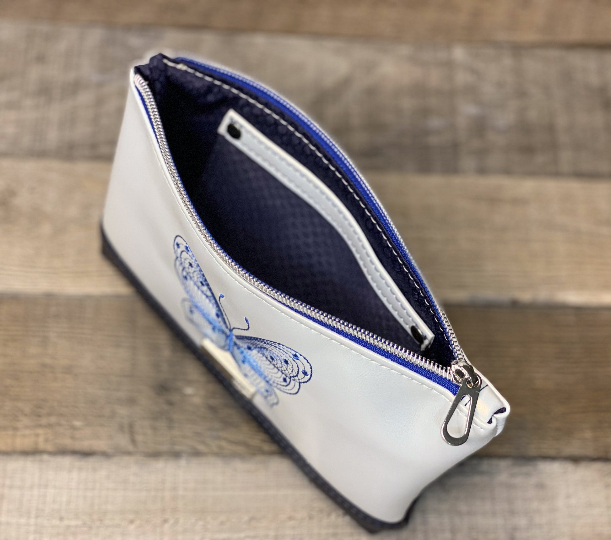 White pouch with blue zipper and butterfly design on a wooden surface
