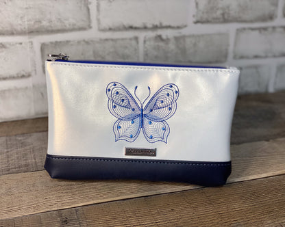 White pouch with blue butterfly design on a wooden surface and brick wall background