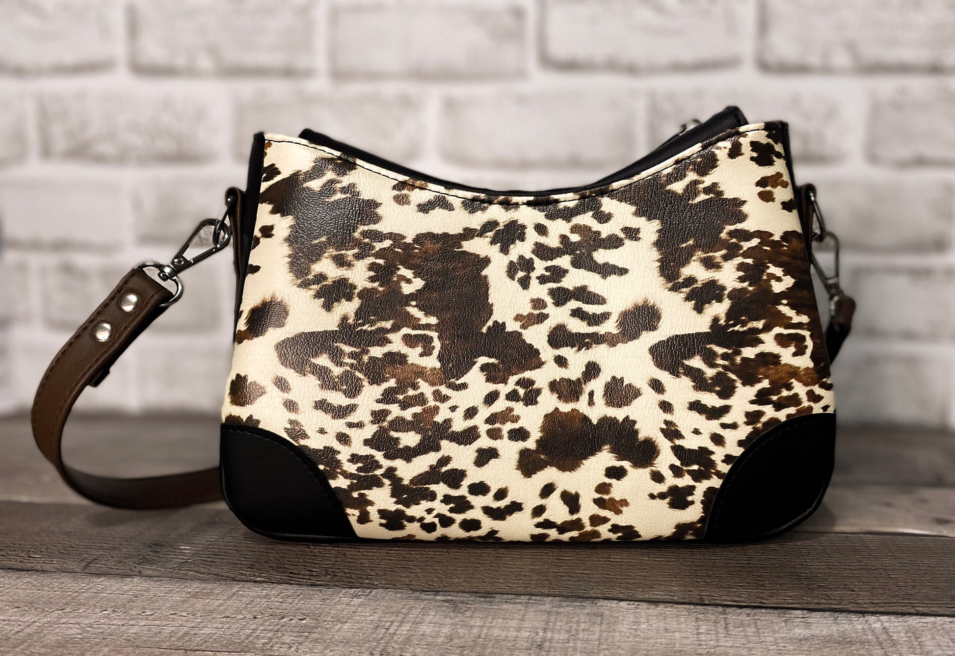 Brown cow print handbag with black faux leather accents. Back view. 