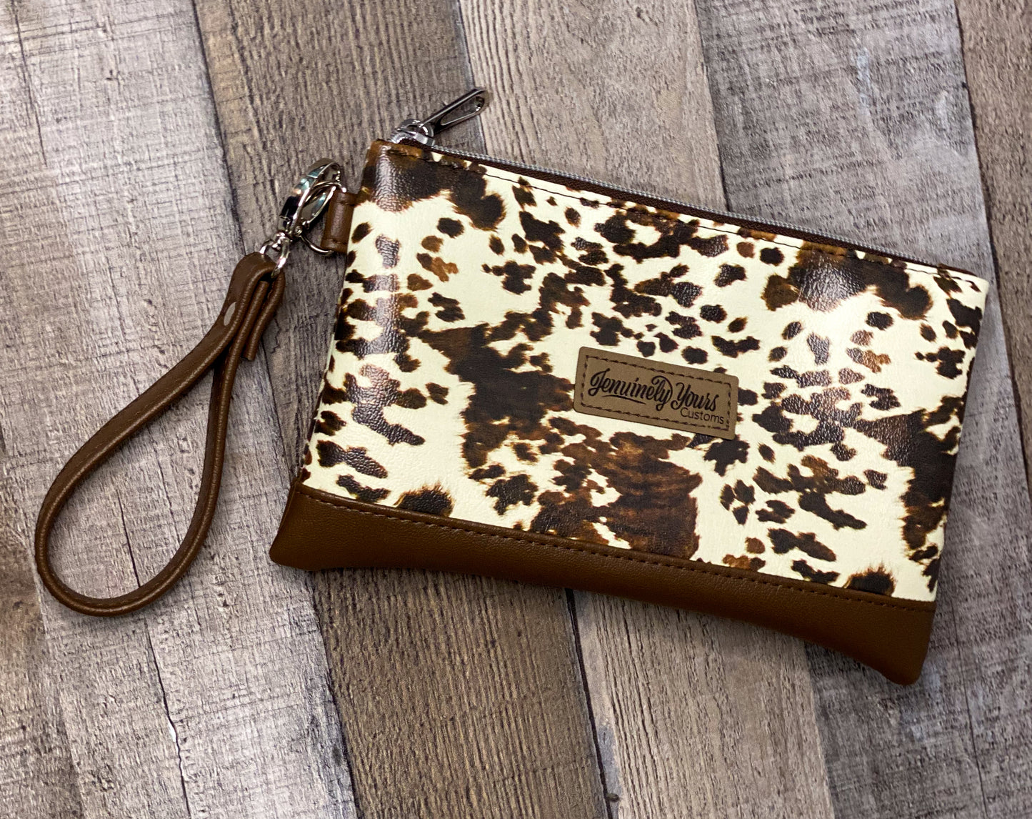 Cow print wristlet with brown strap on a wooden surface