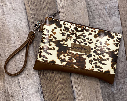 Cow print wristlet with brown strap on a wooden surface