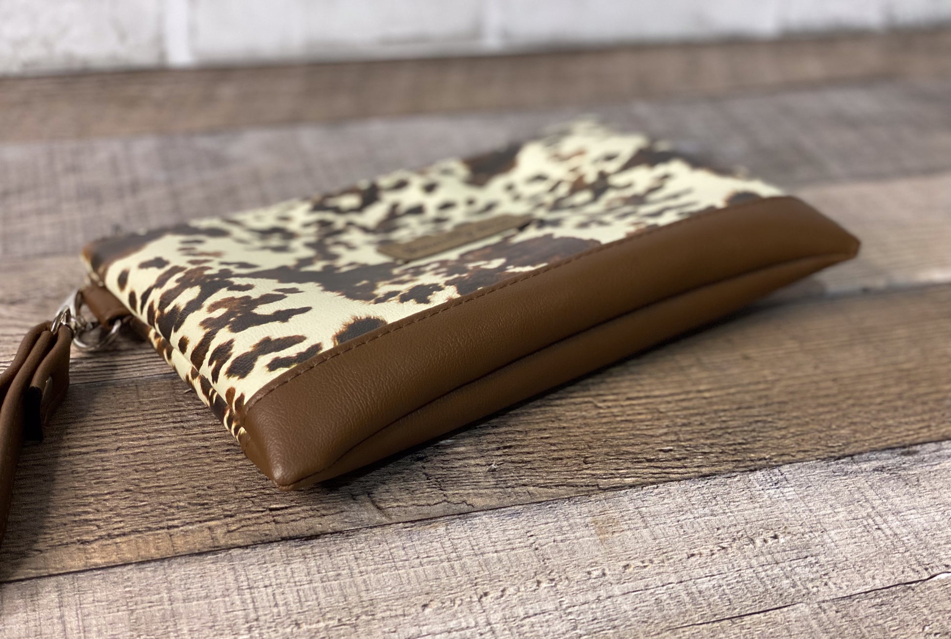 Cow print wristlet with brown strap on a wooden surface