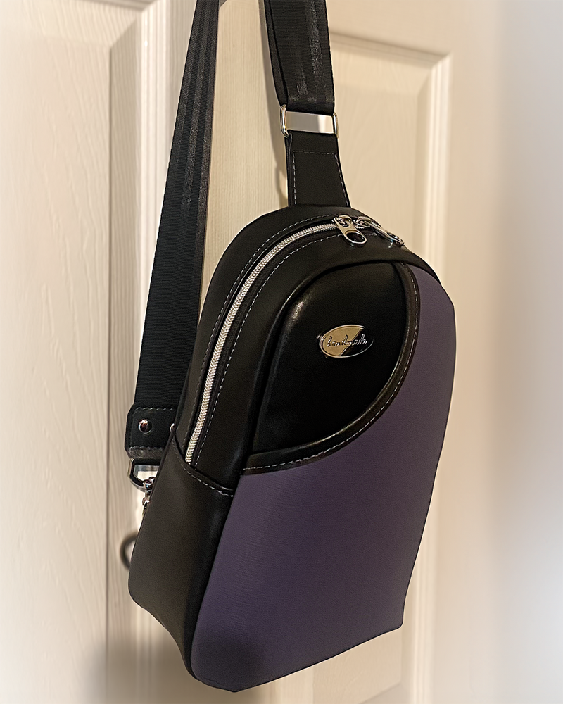 Black faux leather sling bag with purple accent front slip pocket. Seatbelt webbing for the adjustable strap. 